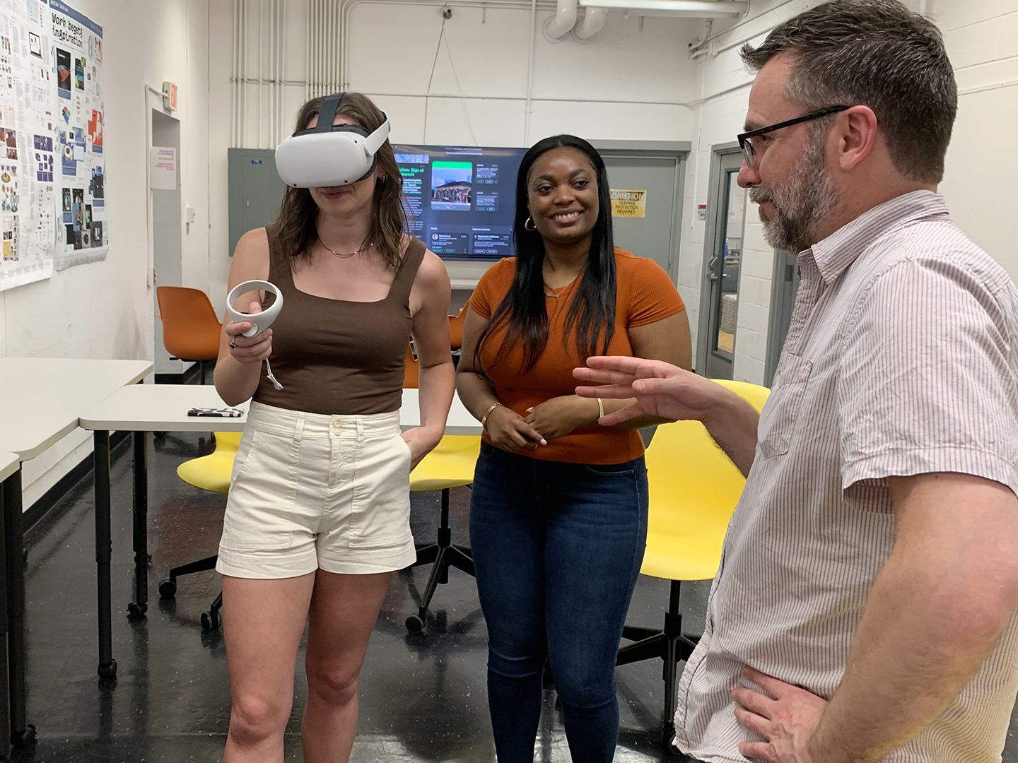 Two college students and a professor discussing a VR experience. One student is wearing a VR headset