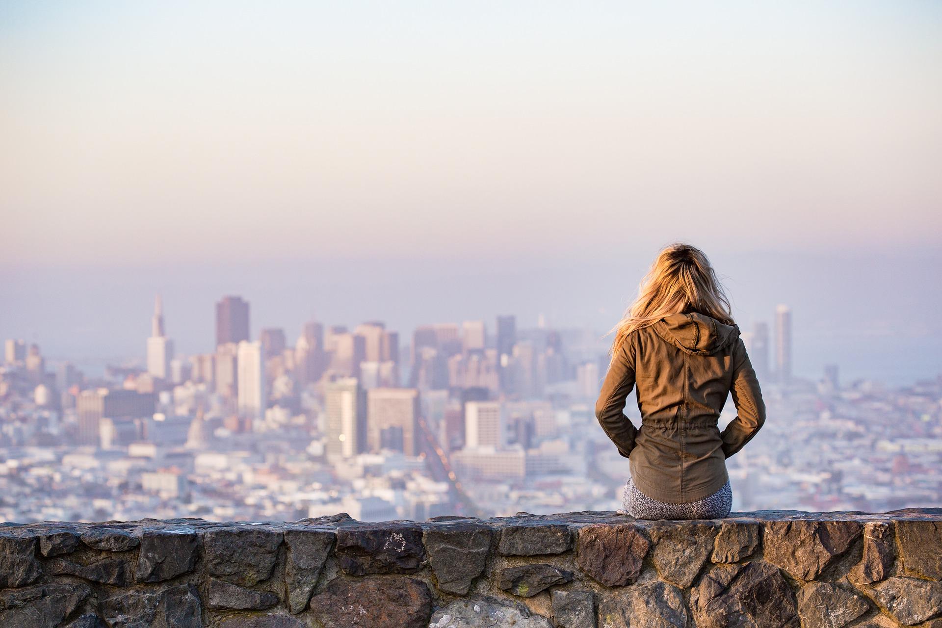Woman sitting on wall looking at city