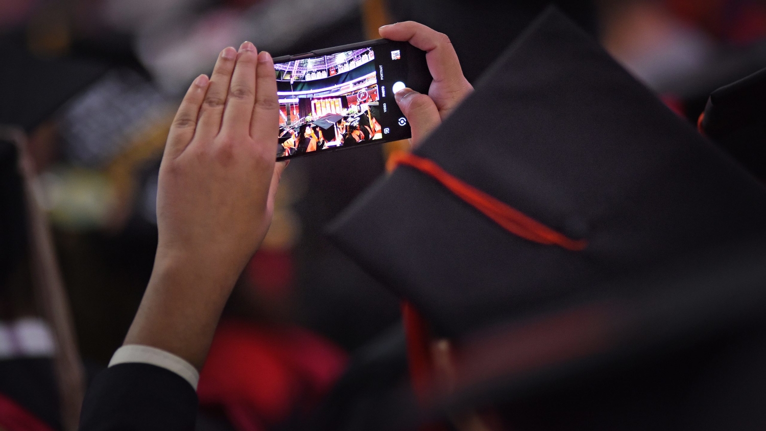 A graduate student takes a cell phone photo at the commencement ceremony