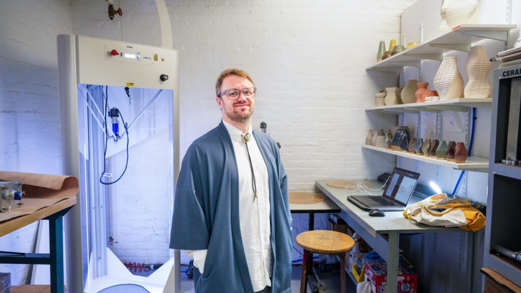 Shawn Protz in the ceramics lab, with 3D printer on his right.