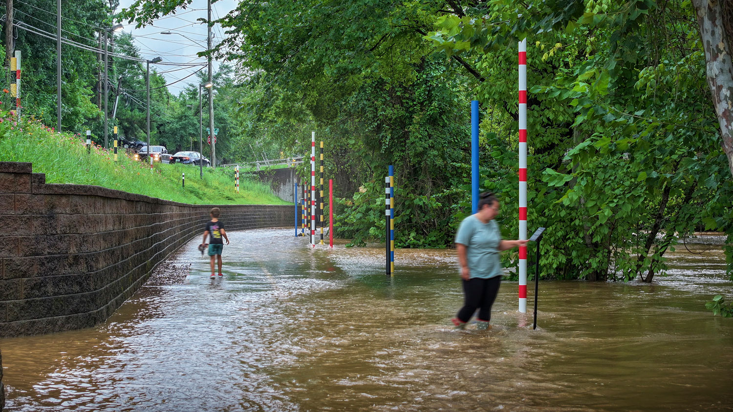 People standing in water-flooded path next to pole markers