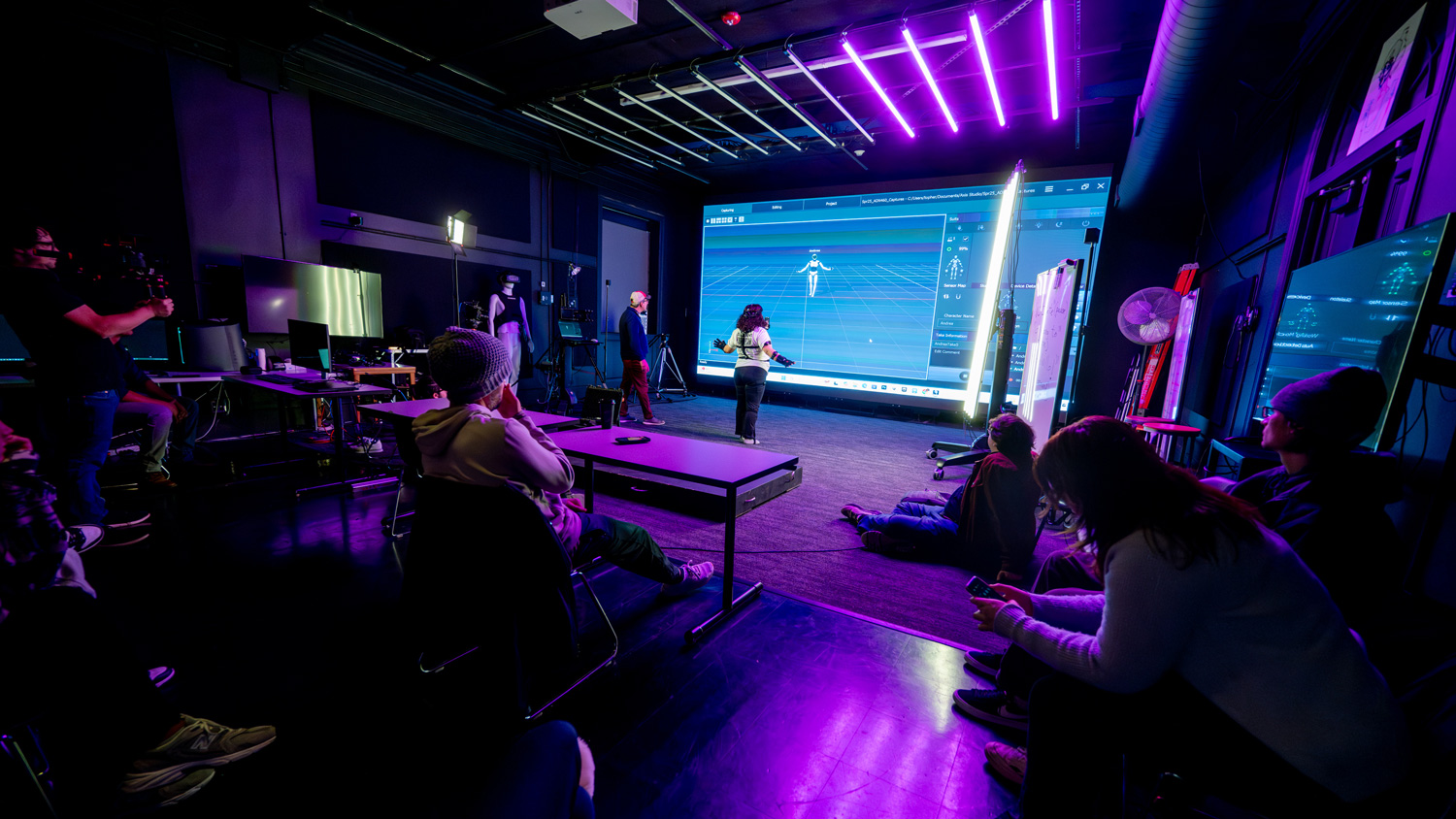 Maraffi instructs students on how to use the motion capture suit in front of the LED wall of the Virtual Production Lab.