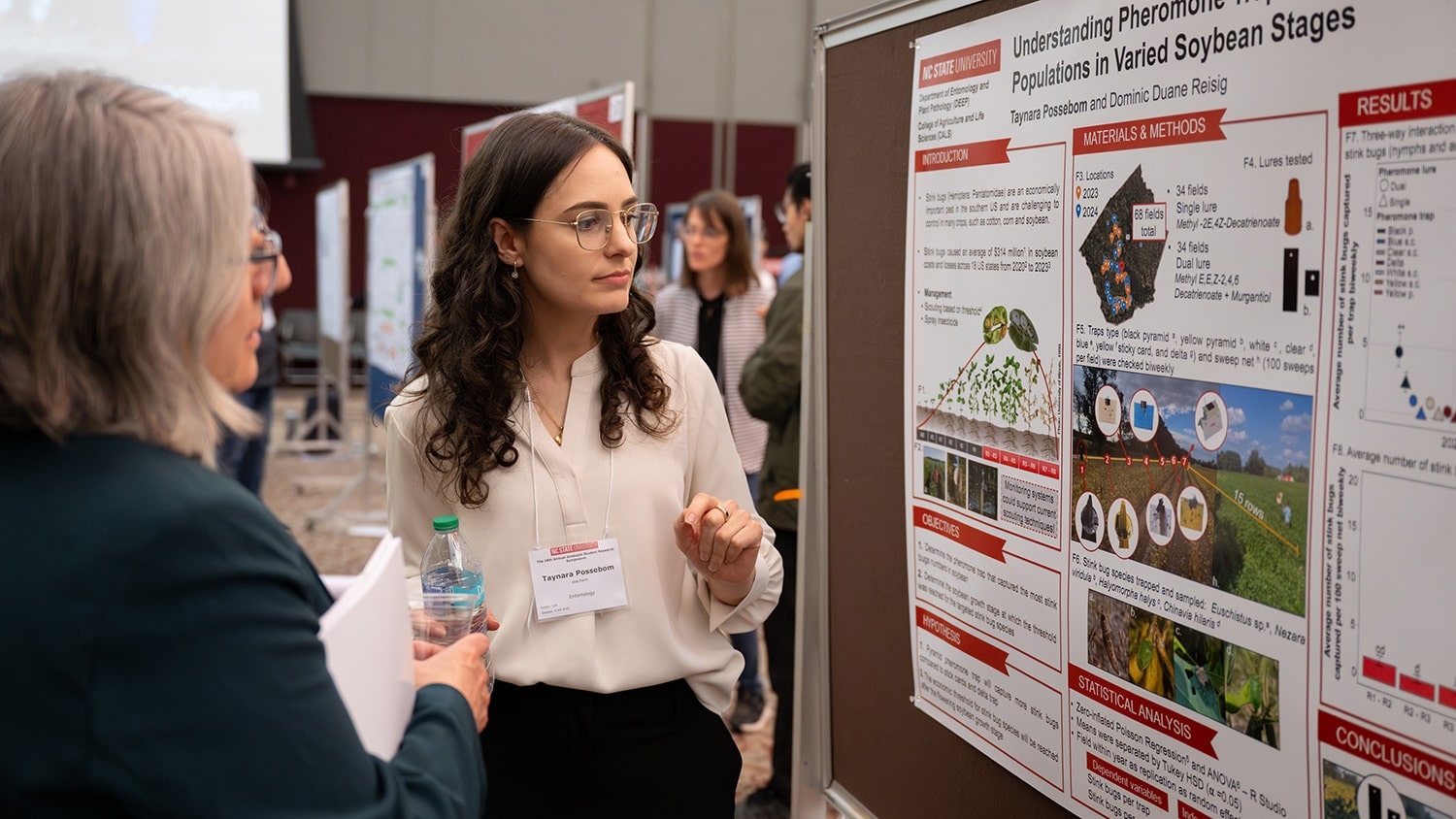 Graduate student Taynara Possebom walks a visitor through her research poster display at the Graduate Student Research Symposium.
