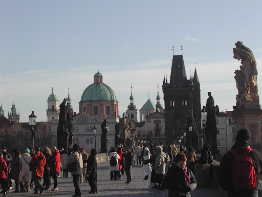 Tourists and locals cross the Charles Bridge in Prague amidst intricate old architecture.